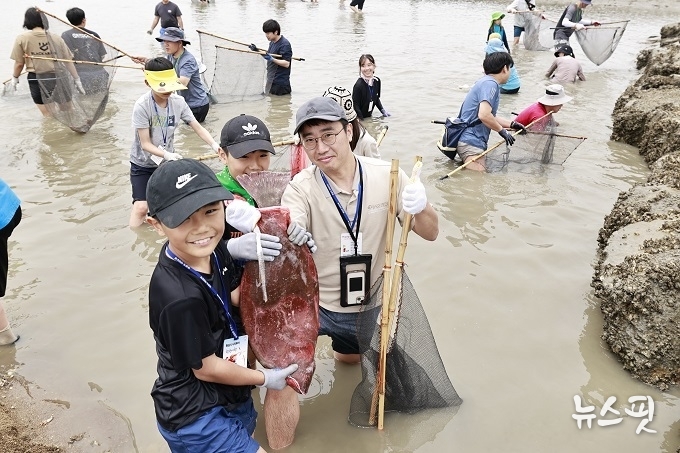 화성 뱃놀이 축제의 ‘독살 체험’ 프로그램에 참여한 가족이 직접 잡은 물고기를 들고 환하게 웃고 있다.(화성특례시 제공)